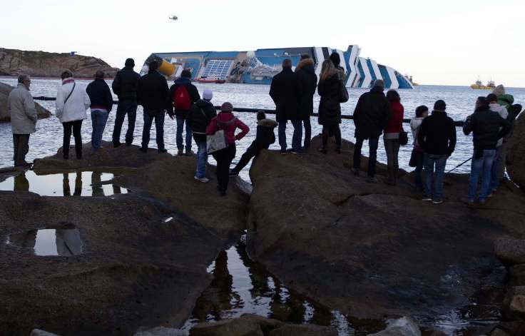 Tourists stand on rocks to see the Costa Concordia cruise ship off Giglio Island