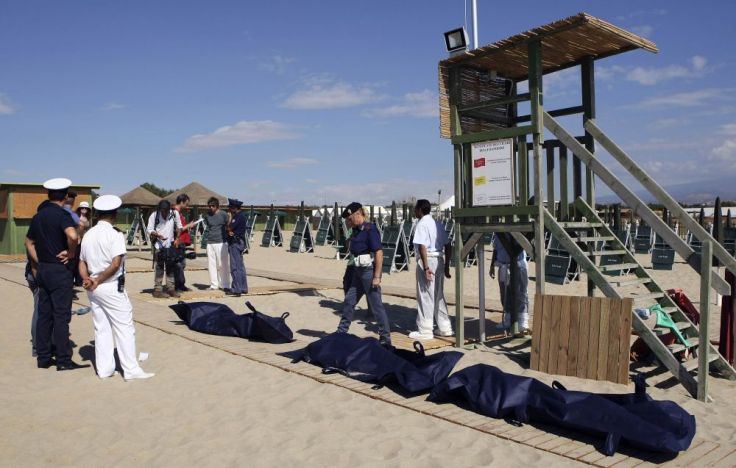 Italian police stand guard next to bodies of migrants who drowned after a shipwreck, at La Playa beach in Catania on Sicily island